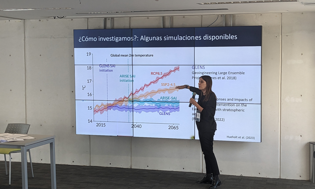 Woman standing in front of presentation slide. She is speaking into a microphone to an audience