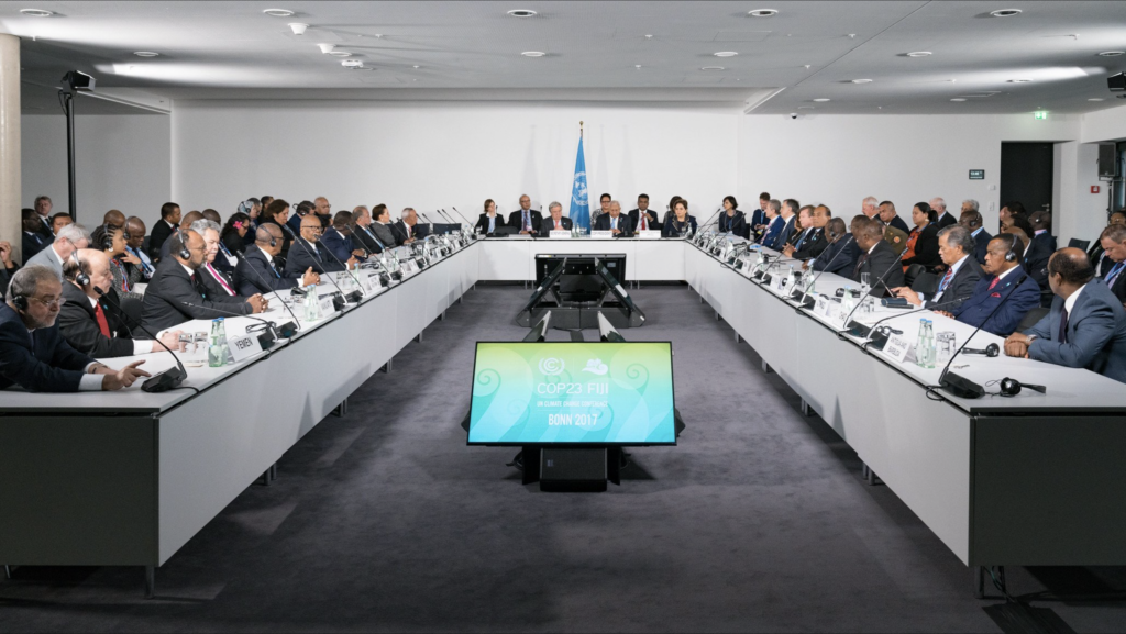 Image of a full UNFCCC meeting room. Delegates listening to a speech using their headphones
