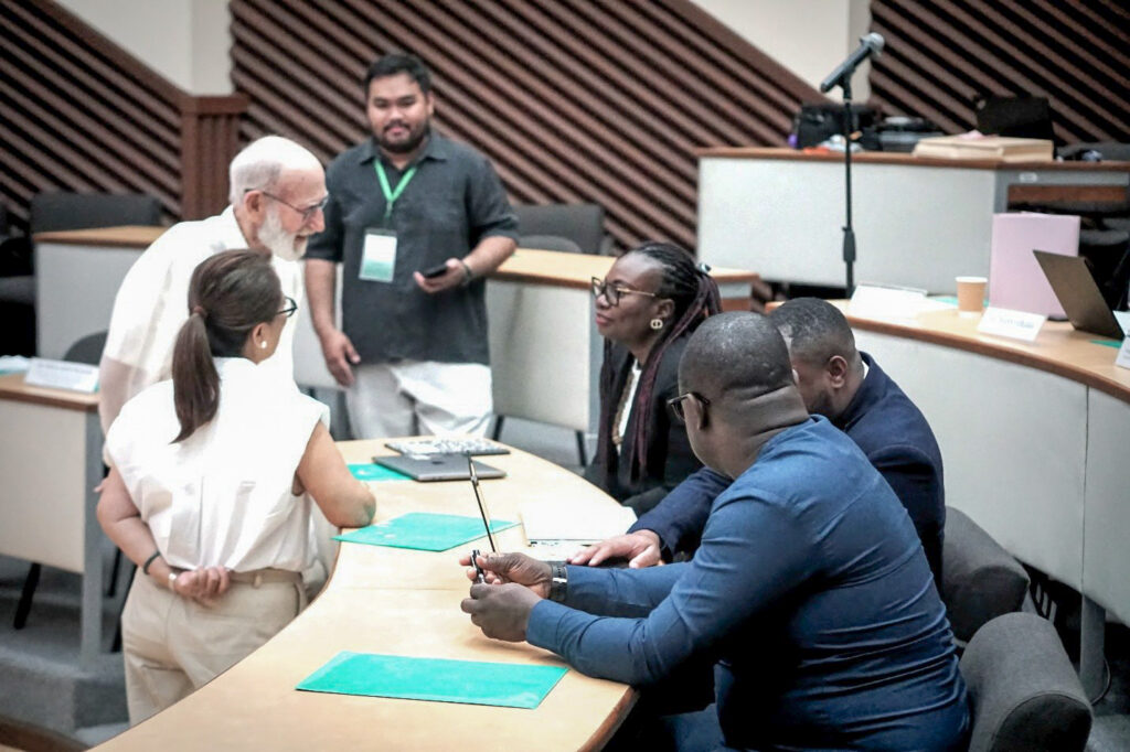 Three people sitting behind a desk with two people leaning over to talk to them