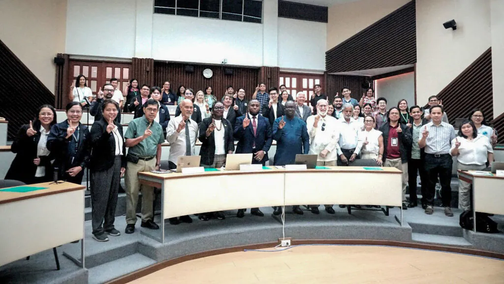 Large group of people in a lecture theatre all holding up one index finger