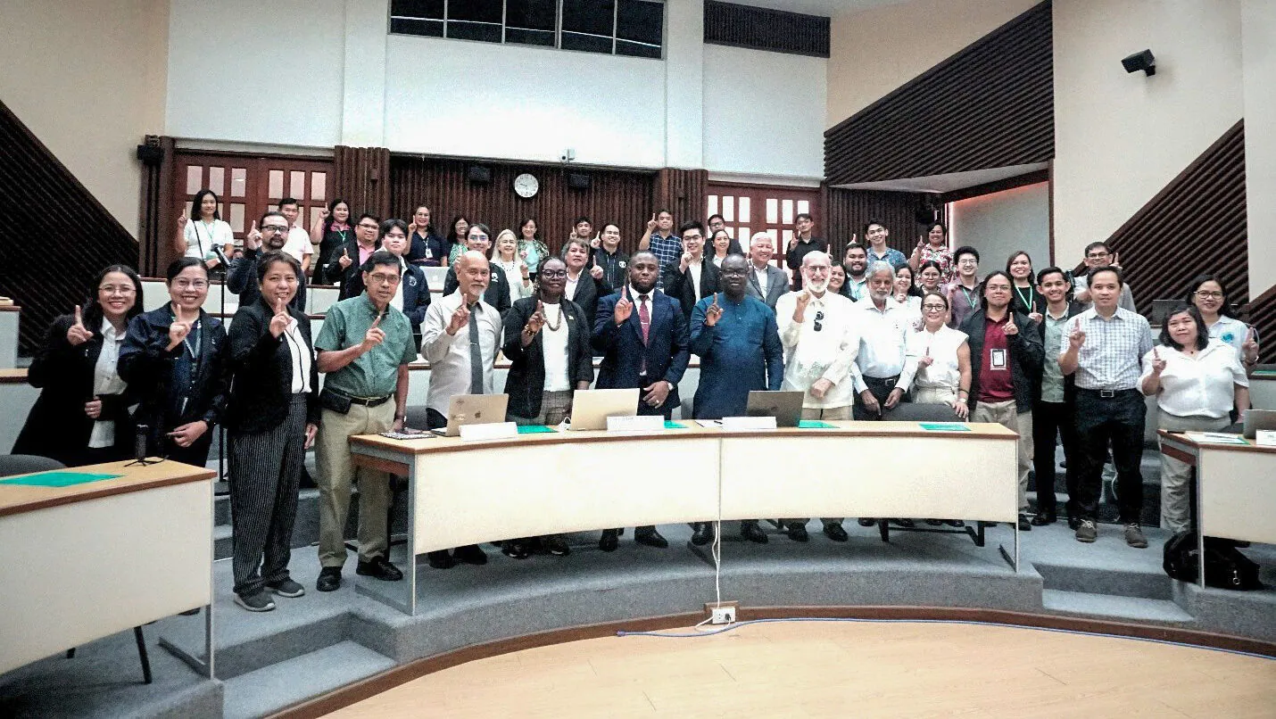 Large group of people in a lecture theatre all holding up one index finger