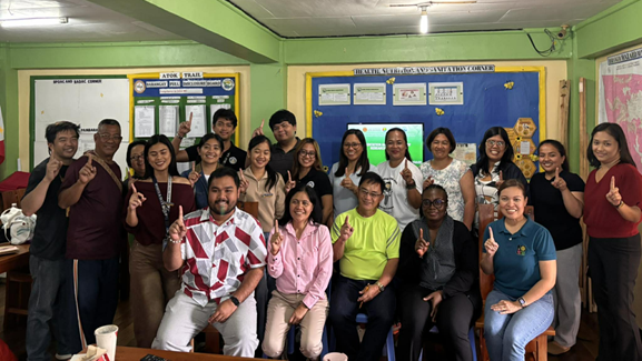 Group of people in a classroom all holding up one index finger